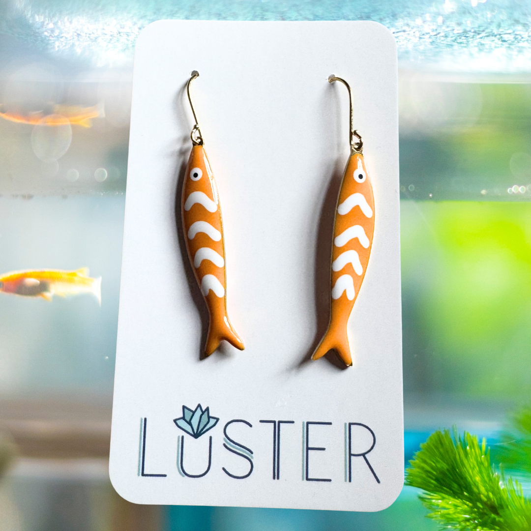 Fish-shaped earrings on a Luster branded card with an aquarium background