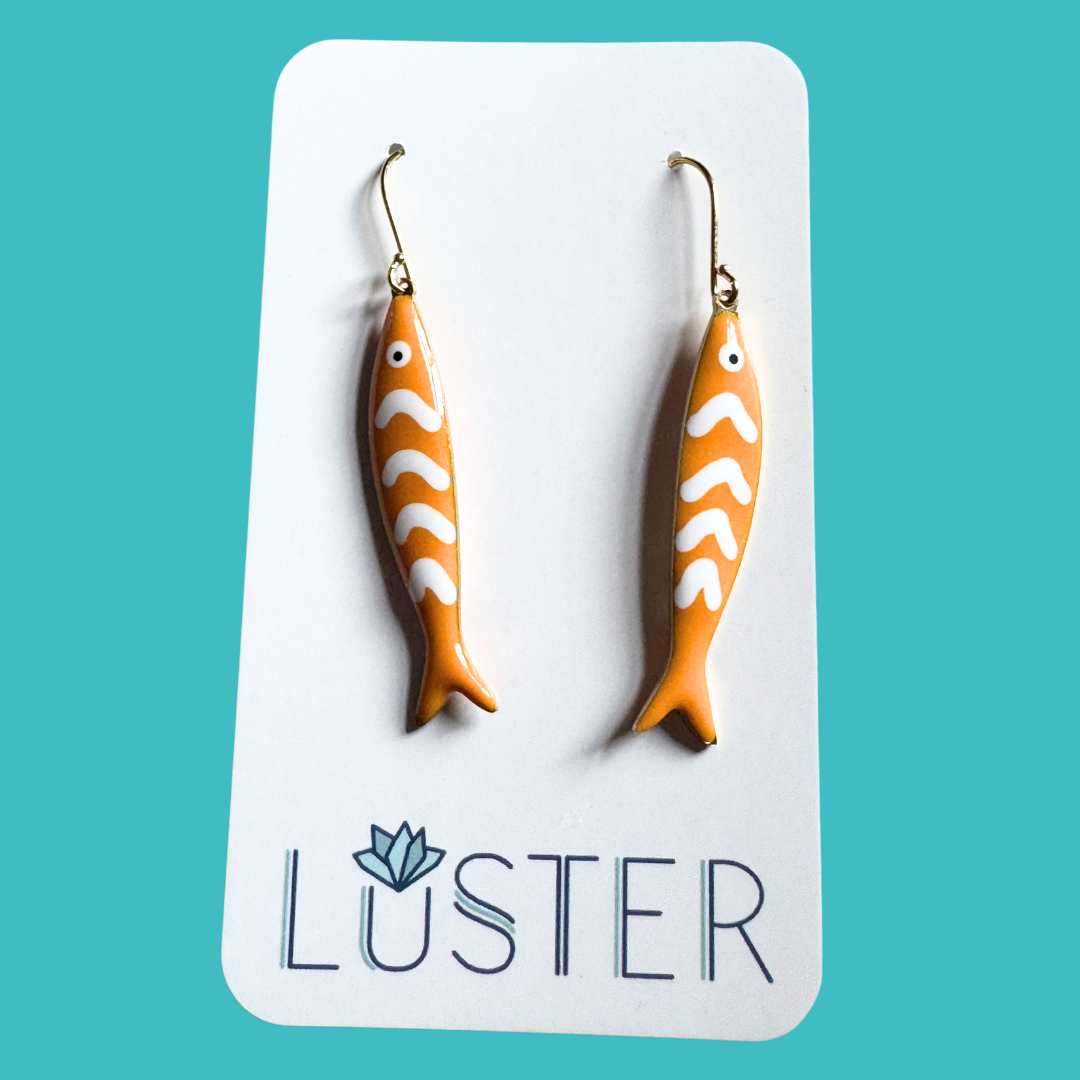 Orange fish-shaped earrings on a Luster branded card against a teal background