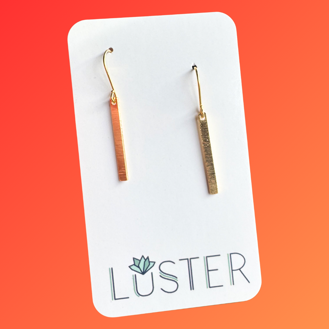Gold bar earrings on a Luster branded card against an orange background