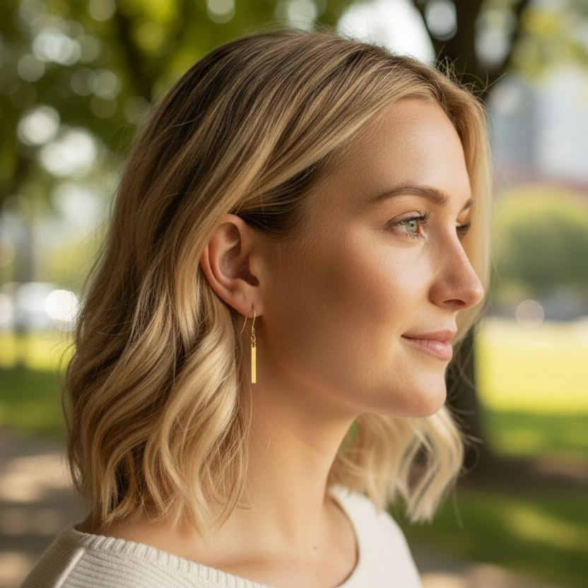 Woman with blonde hair and earrings standing outdoors with trees and buildings in the background