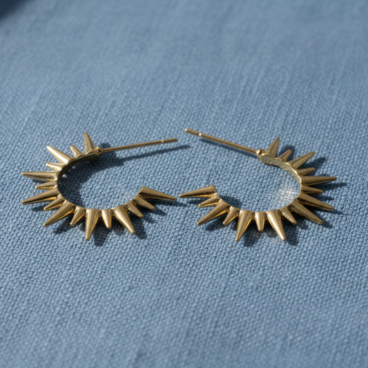 Pair of gold hoop earrings with star-like spike details on a blue fabric background
