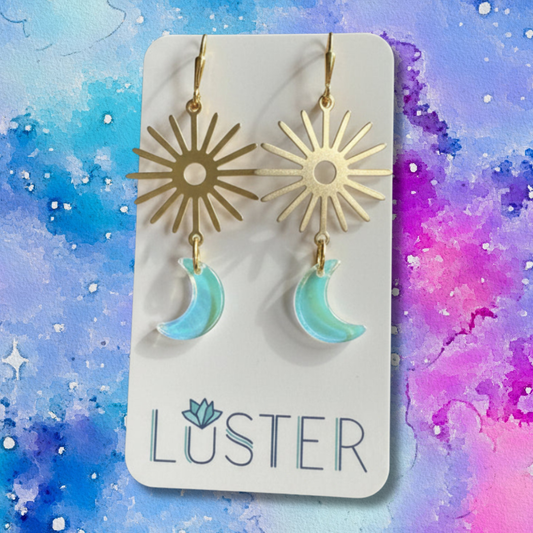 Gold sun and moon earrings on a Luster branded card with a colorful watercolor background