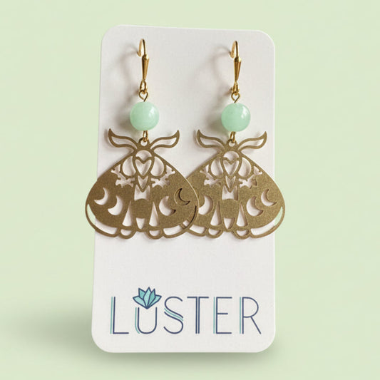 Gold moth earrings with green beads on a Luster branded card