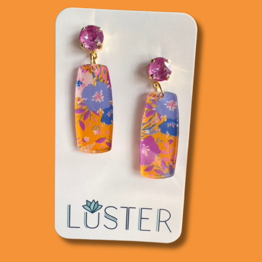 Colorful floral earrings on a Luster branded card against an orange background