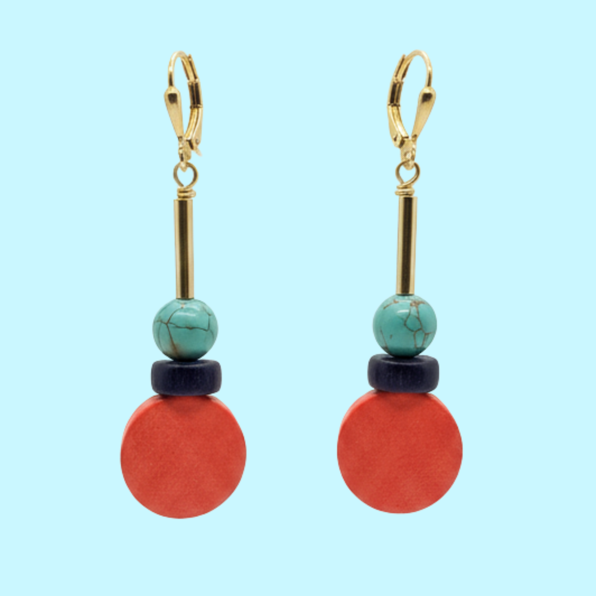 A pair of drop earrings with gold leverback hooks, turquoise beads, dark navy wooden discs, and large round coral-red wooden discs, shown against a solid light blue background.