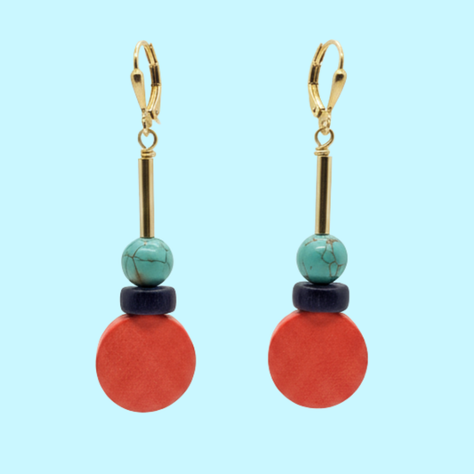 A pair of drop earrings with gold leverback hooks, turquoise beads, dark navy wooden discs, and large round coral-red wooden discs, shown against a solid light blue background.