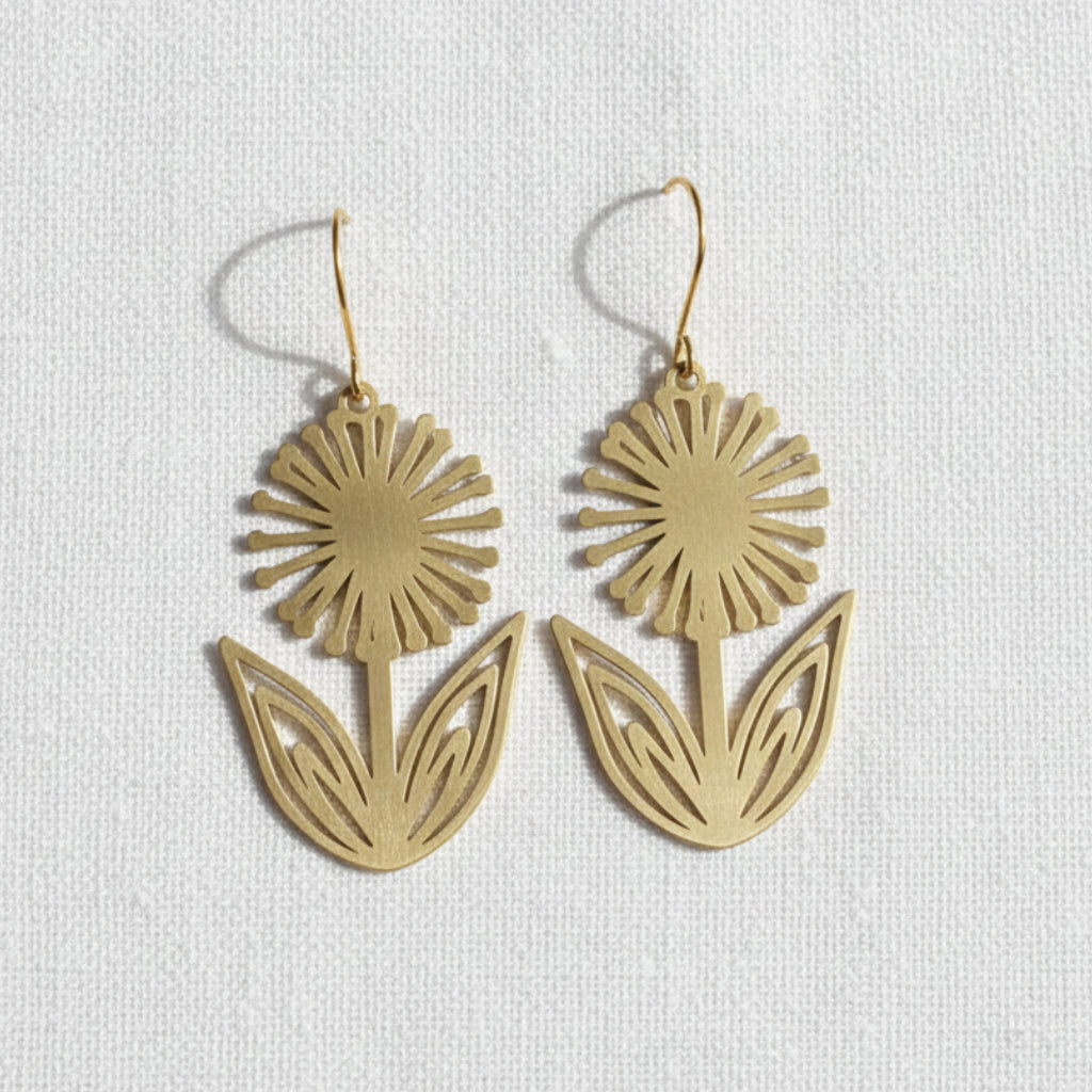 Pair of gold dandelion flower earrings on a light gray background.