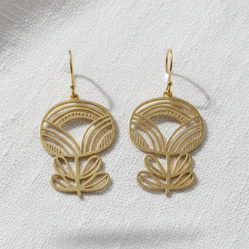 A pair of gold-tone dangle earrings with an intricate openwork floral design, displayed on a textured white fabric background.