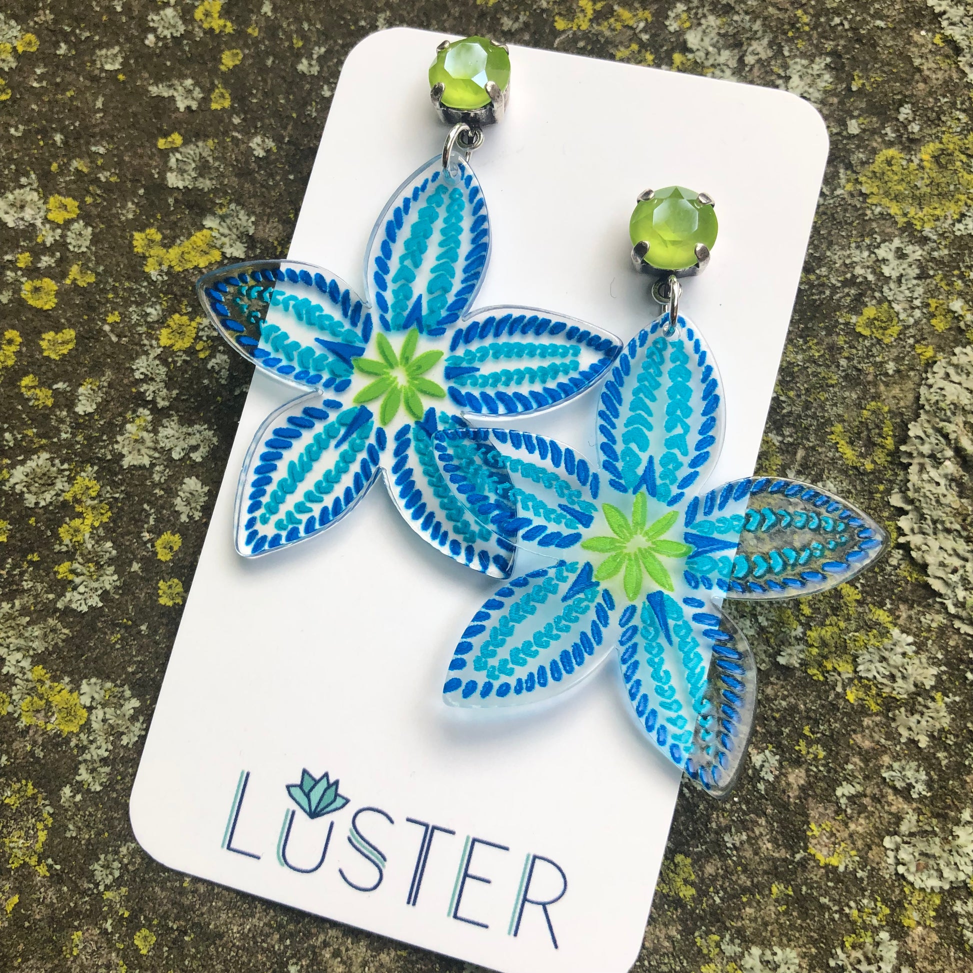 Blue floral earrings on a Luster branded card against a textured background
