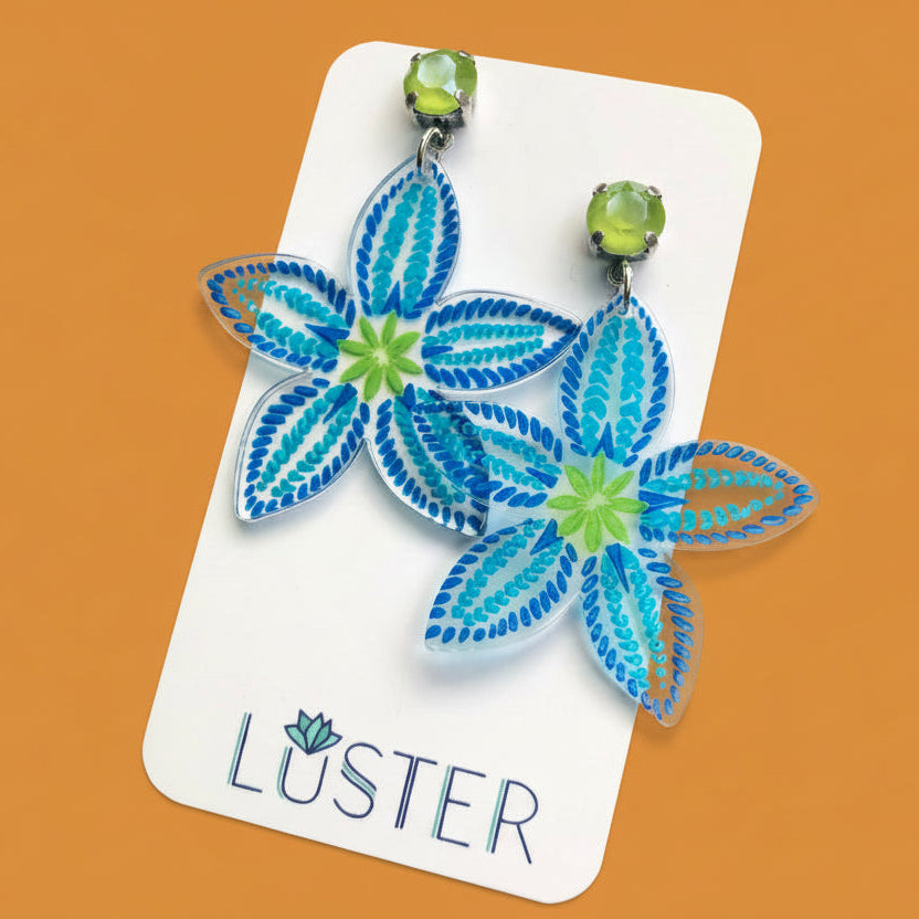 Floral earrings on a Luster branded card against an orange background
