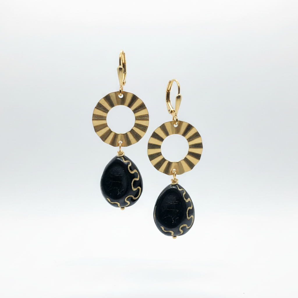 A pair of gold and black drop earrings featuring circular sunburst-patterned rings and teardrop-shaped black beads with gold trim, shown against a clean white background.