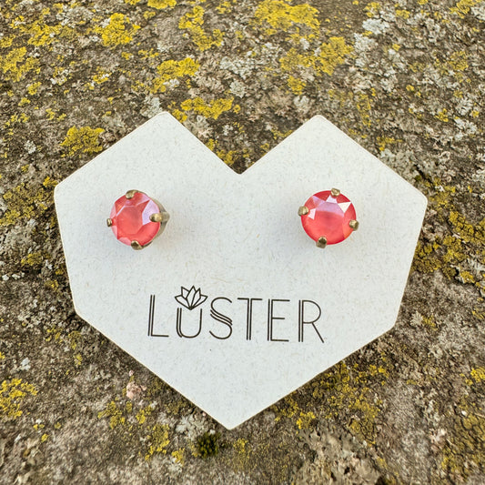 Coral stud earrings on a Luster branded card against a textured stone background
