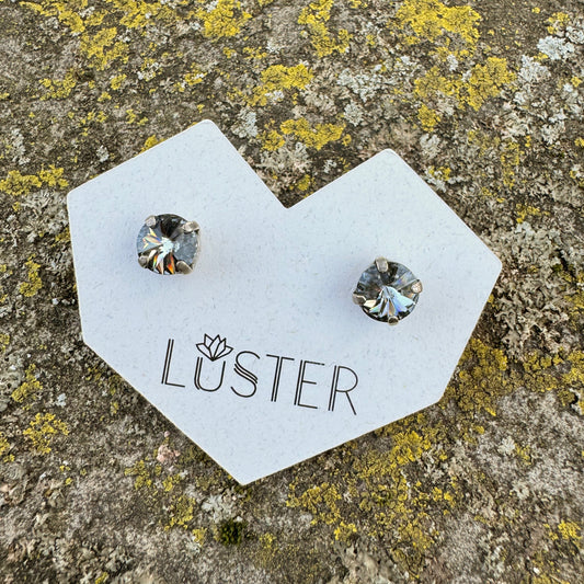 Pair of gray and silver stud earrings on a 'Luster' branded card against a textured stone background.