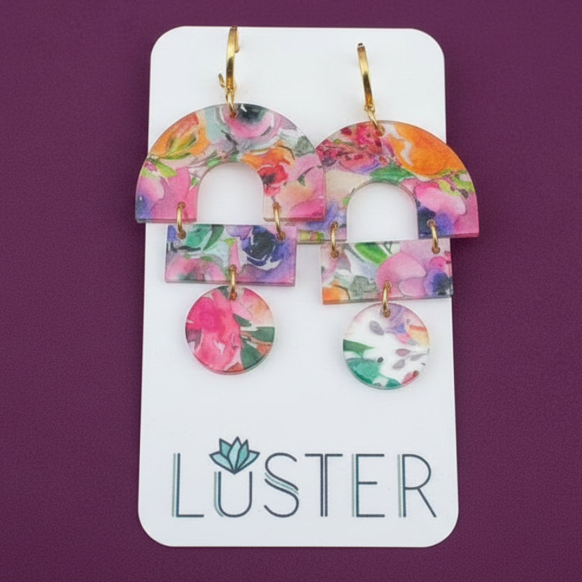 Colorful floral earrings on a Luster branded card against a textured background