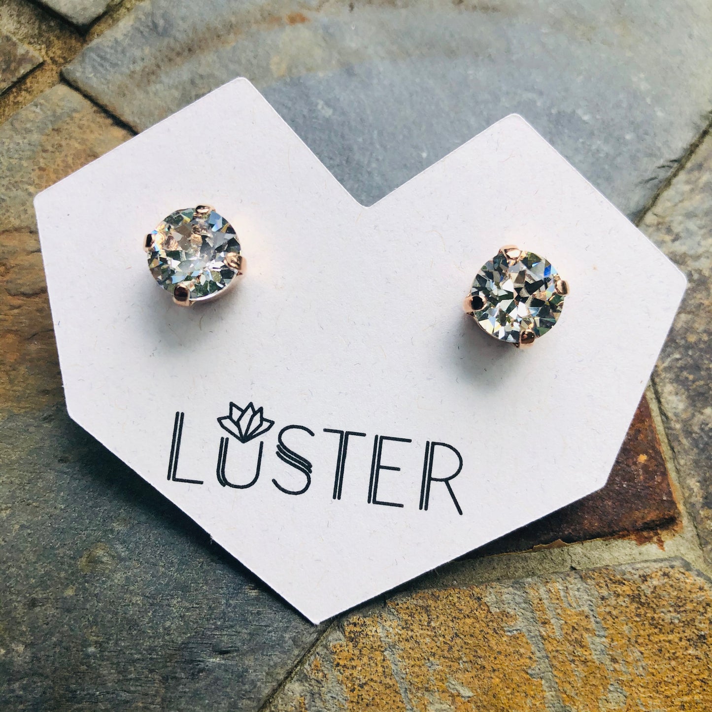 Pair of round crystal stud earrings on a 'Luster' branded card against a stone background