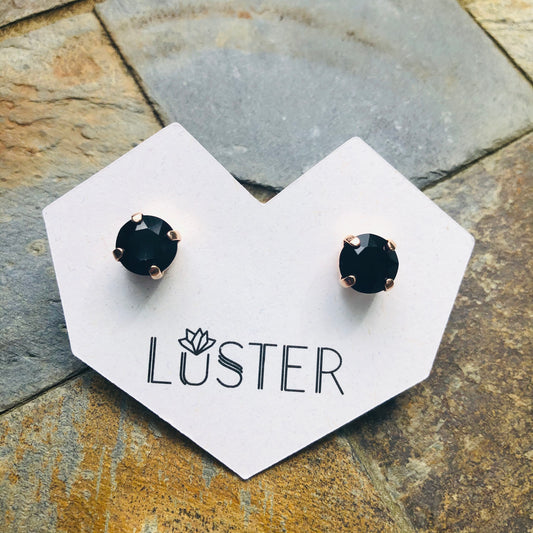 Black stud earrings on a 'Luster' branded card against a stone background