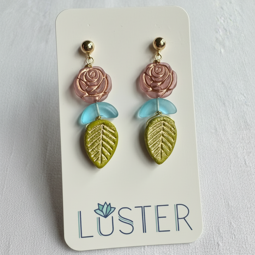 Pair of earrings with rose and leaf design on a Luster branded card.