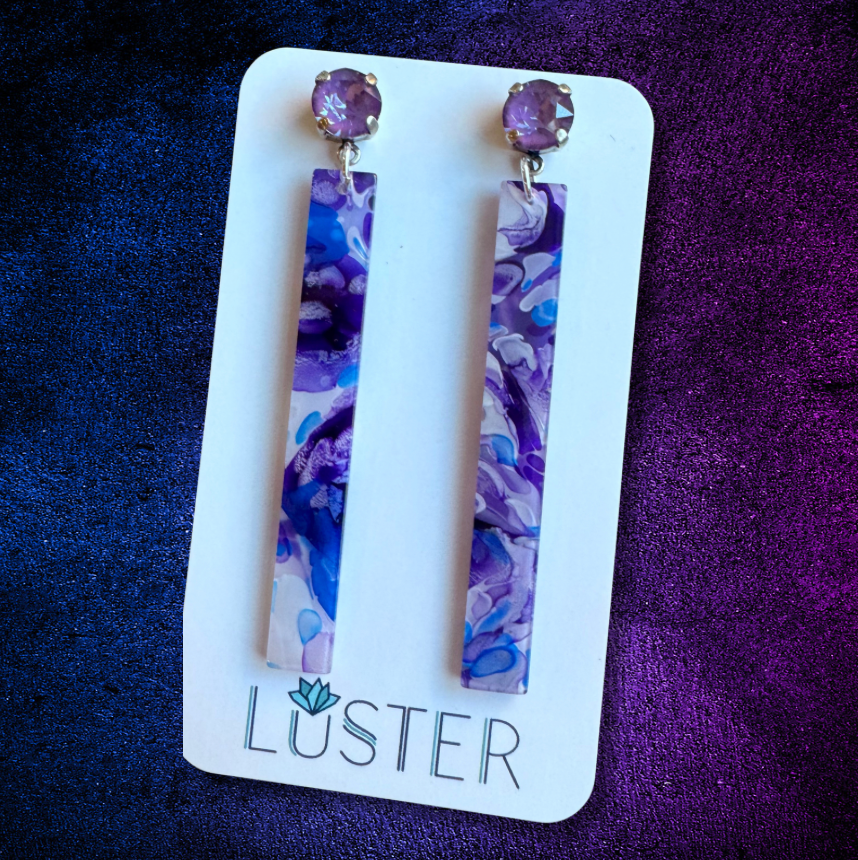 Pair of purple floral earrings on a Luster branded card against a purple background