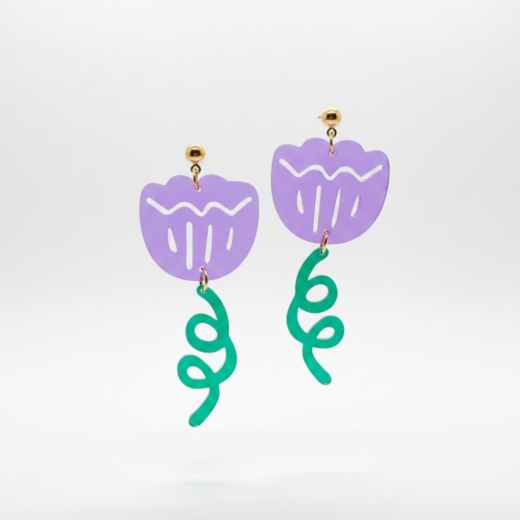 A pair of dangling earrings with light purple flower-shaped tops and bright green curly vine-like drops, shown on a clean light gray studio background.