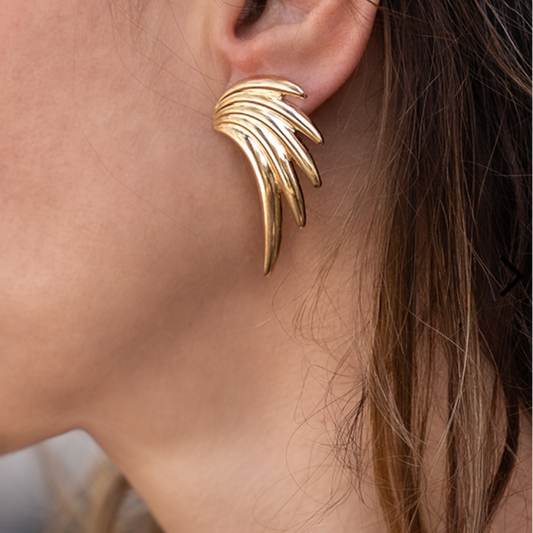 Gold wing-shaped earring worn by a person with blurred background