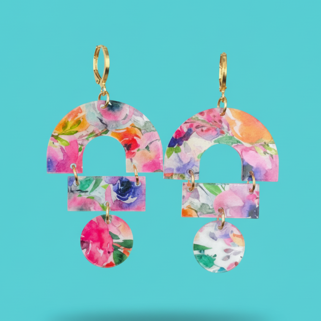 A pair of gold-tone hoop earrings with layered arch and rectangular dangles covered in a colorful floral print, shown against a solid turquoise background.
