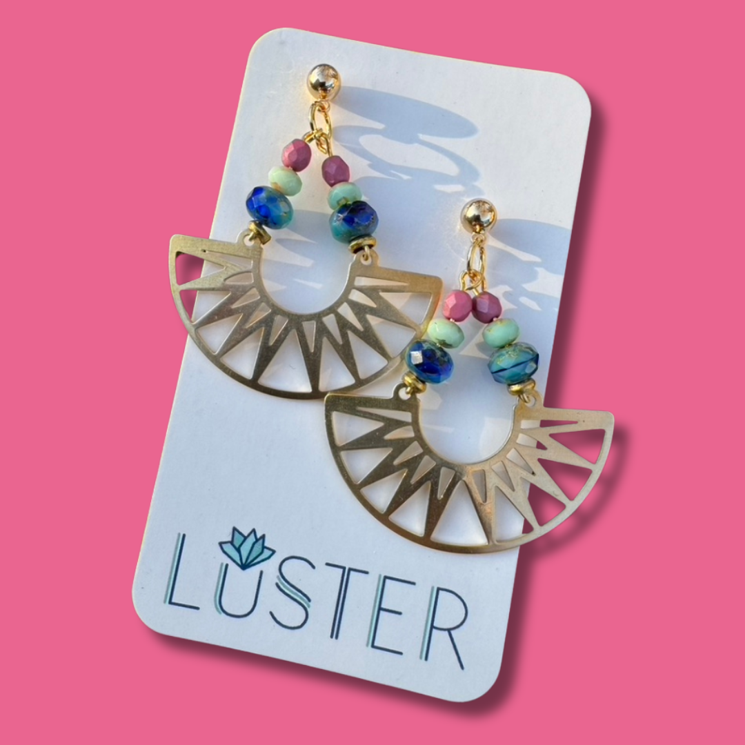 Earrings on a Luster branded card against a pink background