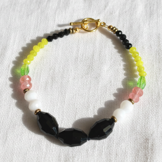 black white pink and green bracelet on white linen background