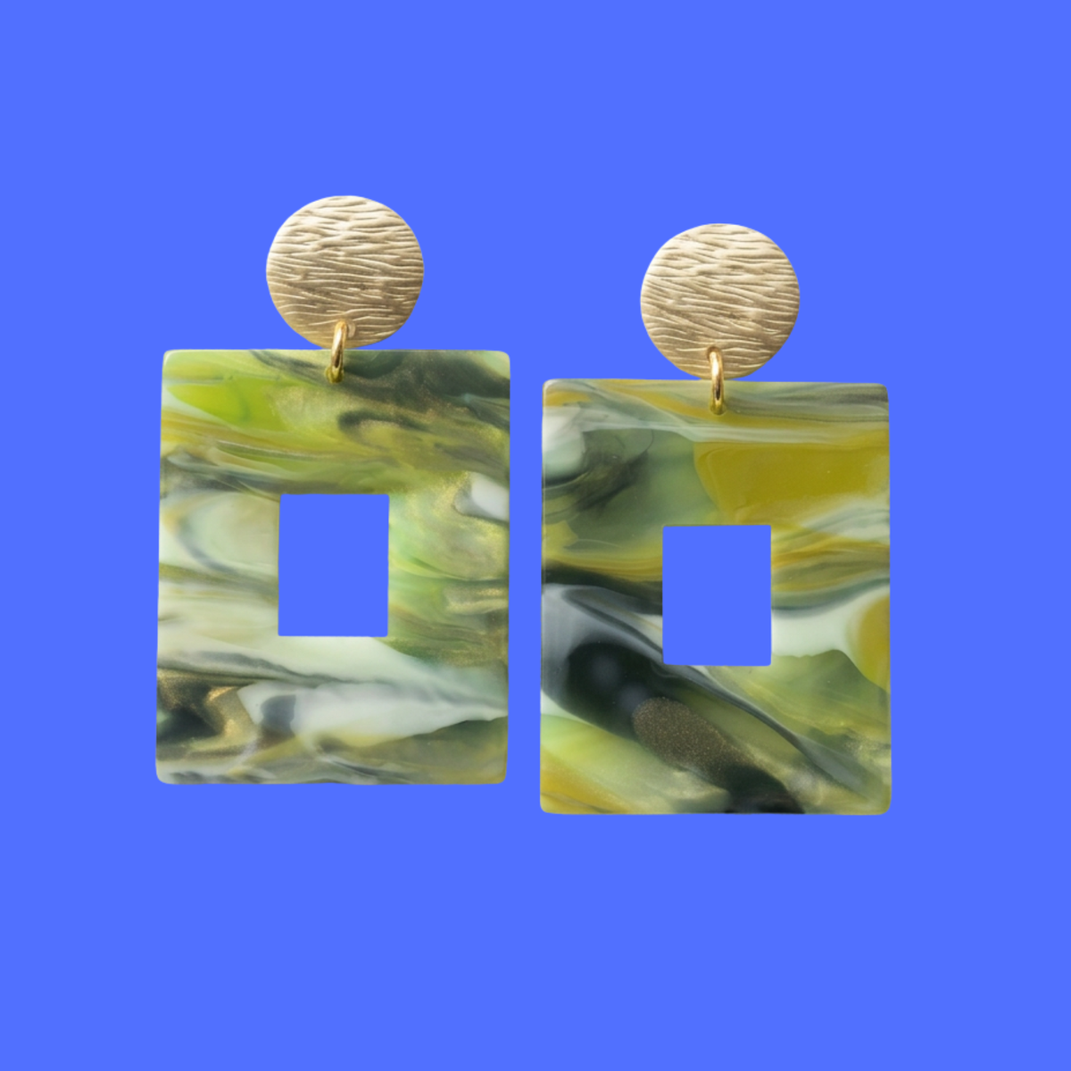 A pair of drop earrings featuring rectangular marbled resin pendants in green, yellow, and white swirls with a square cutout, suspended from round textured gold-tone studs, shown against a solid blue background.