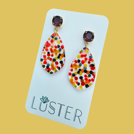 Colorful teardrop earrings on a Luster branded card against a yellow background