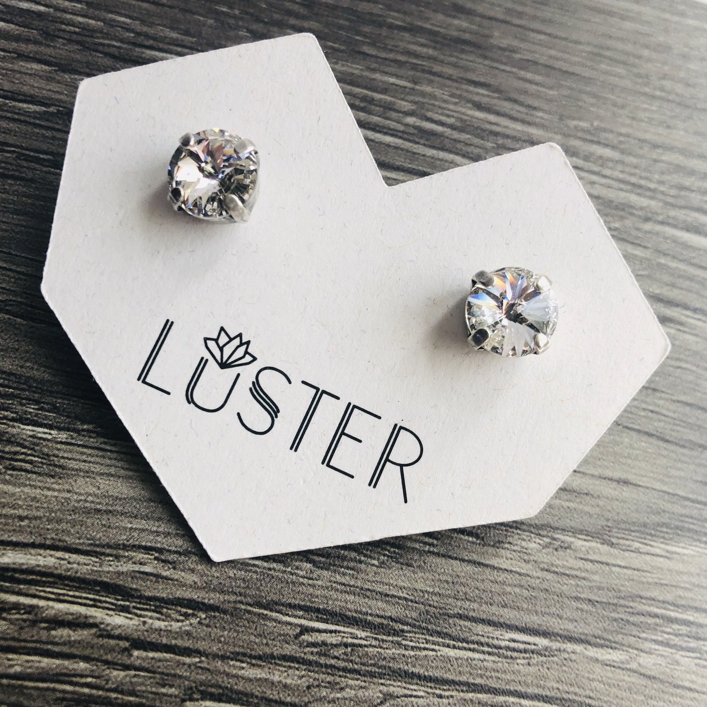 Crystal stud earrings on a Luster branded card with a wood background