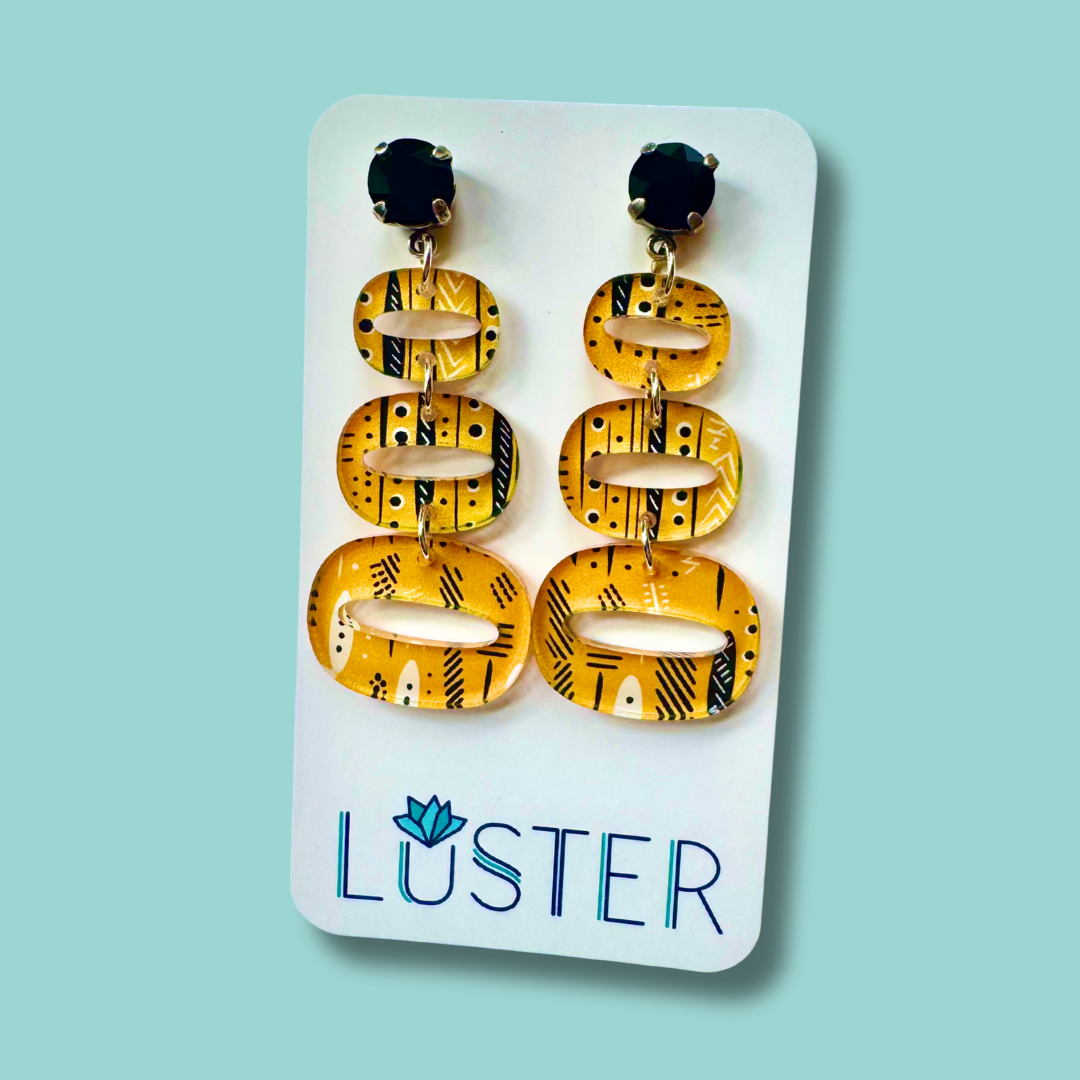 Pair of yellow and black patterned earrings on a Luster branded card against a light blue background