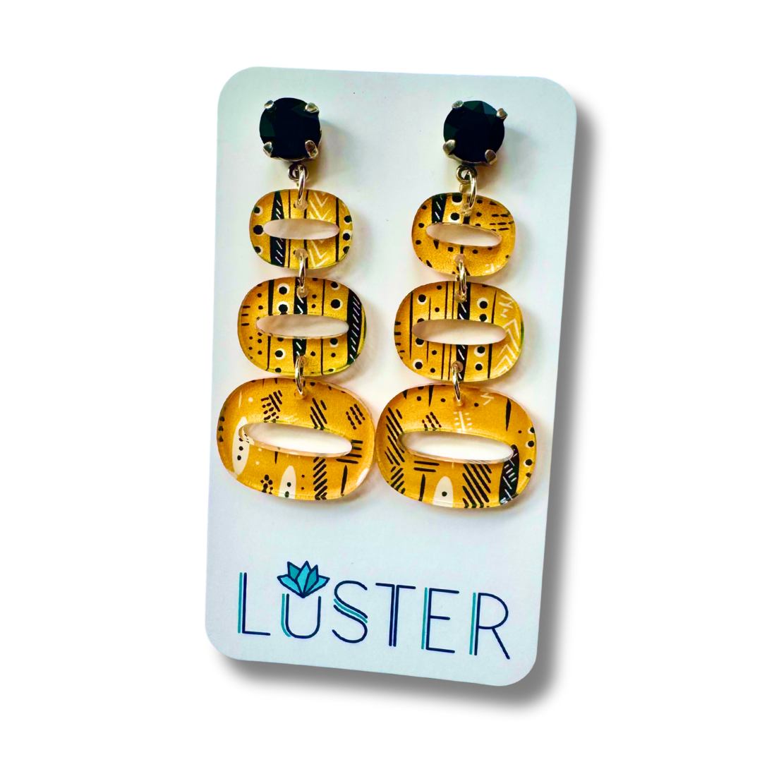 Pair of yellow and black patterned earrings on a Luster branded card.
