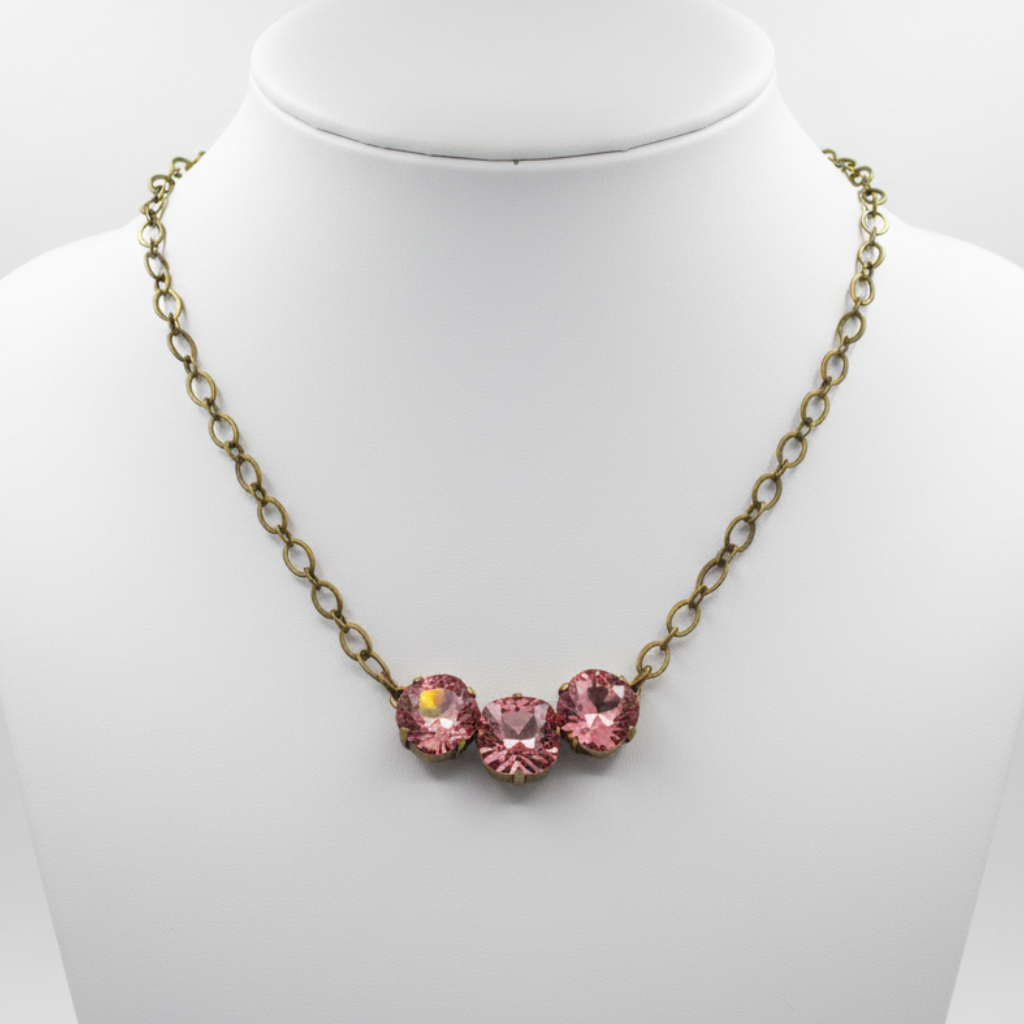 An antique bronze chain necklace with three pink faceted crystal rhinestones in a row, displayed on a white jewelry bust.