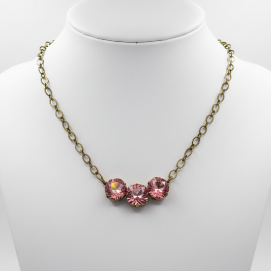 An antique bronze chain necklace with three pink faceted crystal rhinestones in a row, displayed on a white jewelry bust.