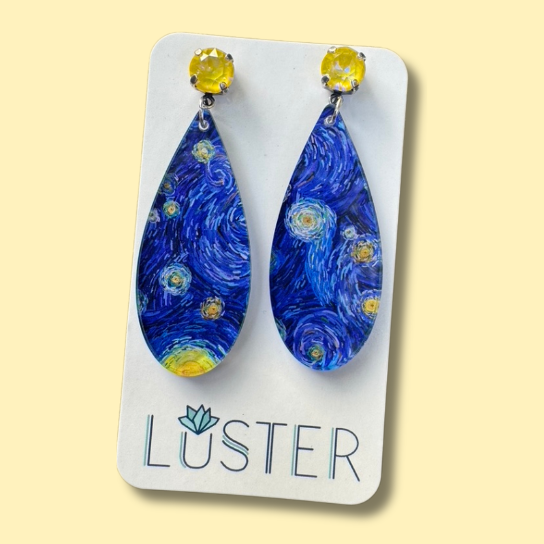 Blue teardrop earrings with yellow accents on a Luster branded card against a beige background