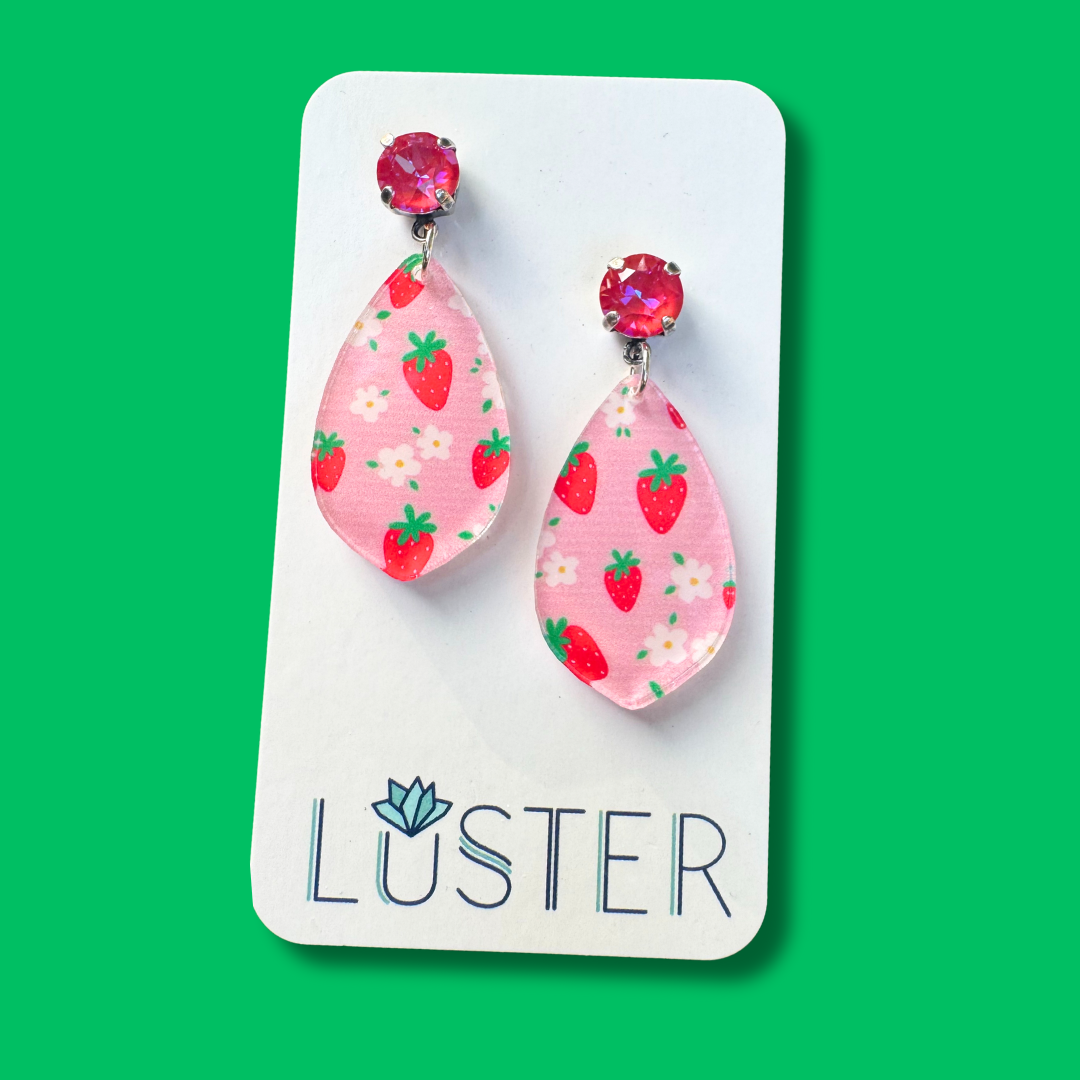 Pink teardrop earrings with strawberry pattern on a Luster branded card against a green background