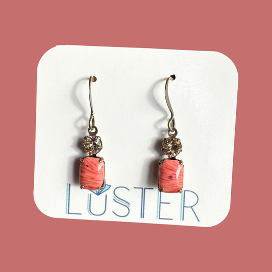 Pair of earrings with coral-colored beads on a Luster branded card against a pink background