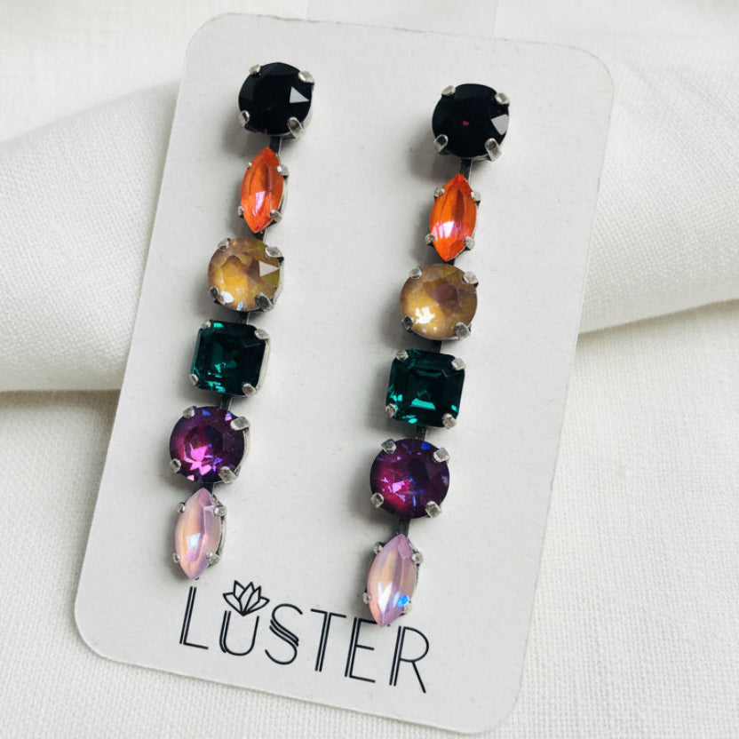 Colorful gemstone earrings on a Luster branded card against a white linen background