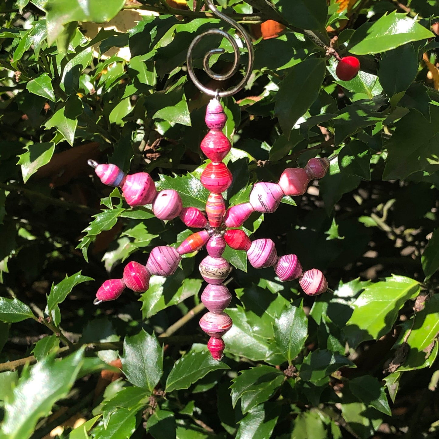 A colorful paper ornament with a star shape and hanging beads, displayed on a bush with green leaves.