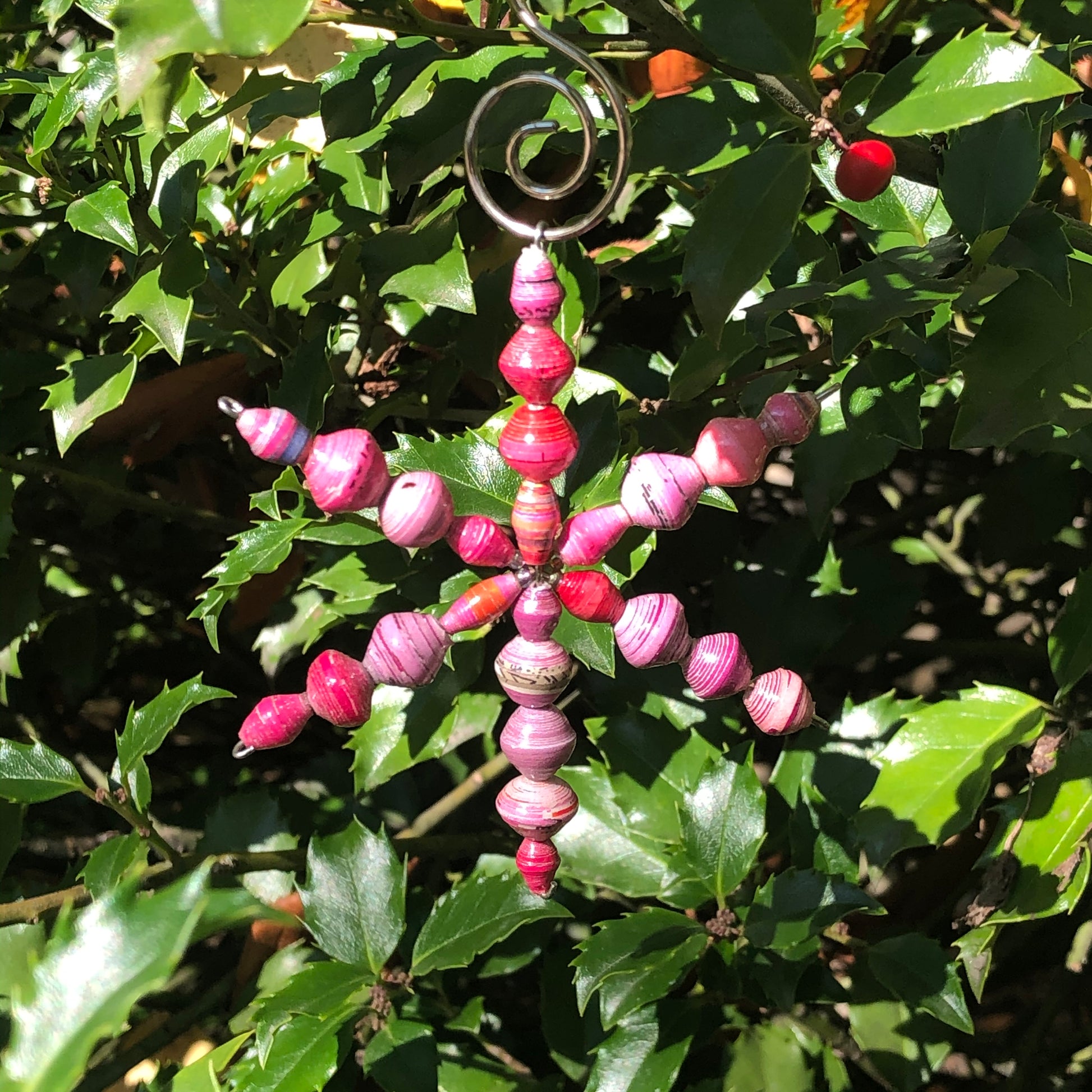 A colorful paper ornament with a star shape and hanging beads, displayed on a bush with green leaves.