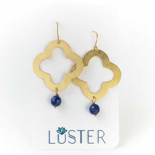 Gold earrings with blue stones on a Luster branded card against a natural background